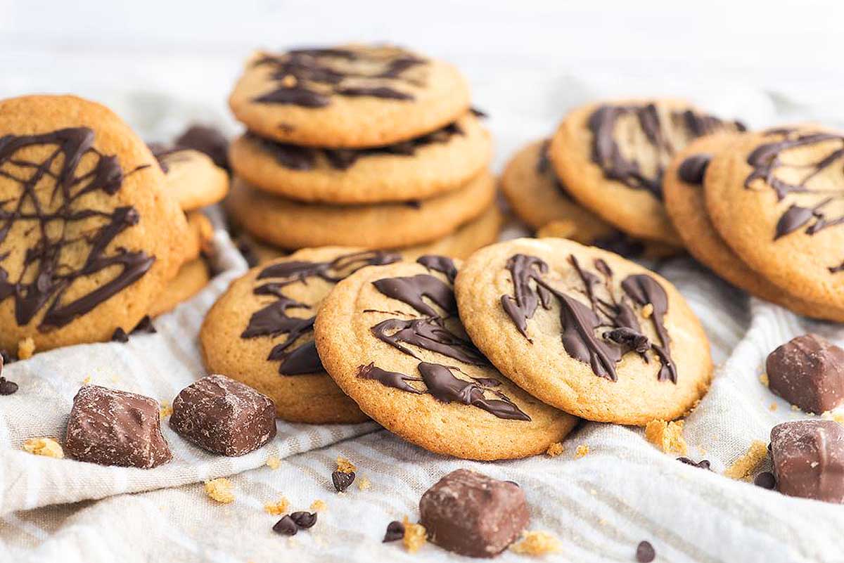 A pile of cookies with chocolate drizzle on a napkin.