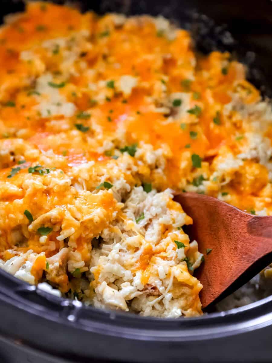 a wooden spoon lifting crockpot chicken and rice from a crockpot. 
