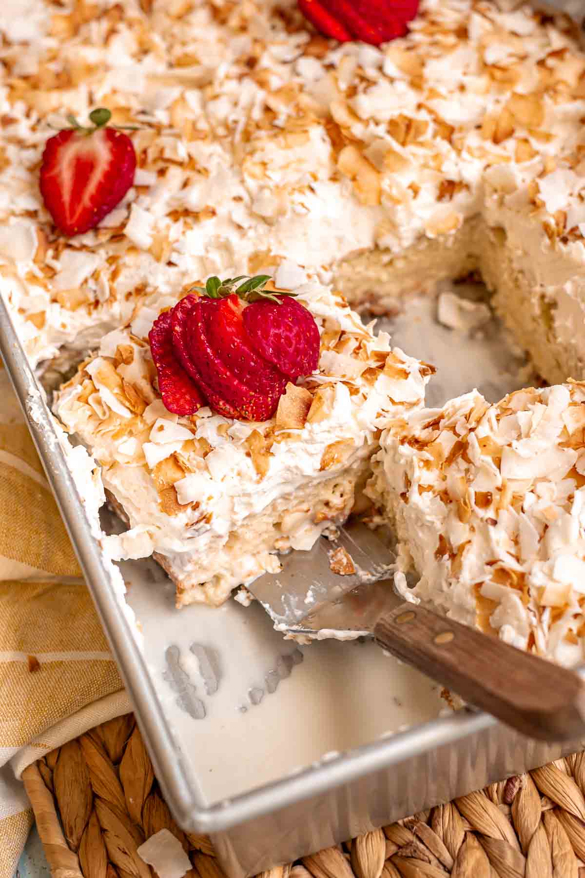 A spatula removes a soaked piece of coconut tres leches cake from a pan.